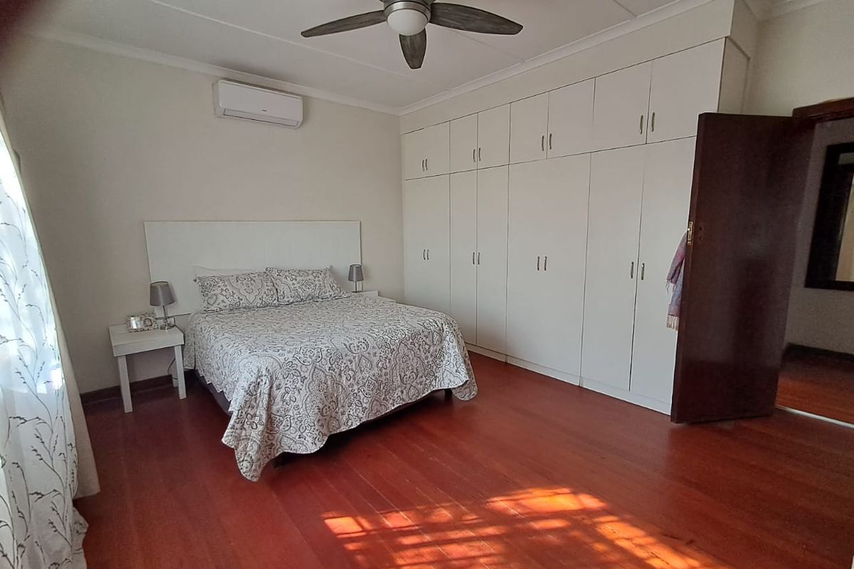A well-maintained bedroom featuring polished timber flooring, extensive built-in cabinetry, a ceiling fan, and a wall-mounted air conditioning unit.