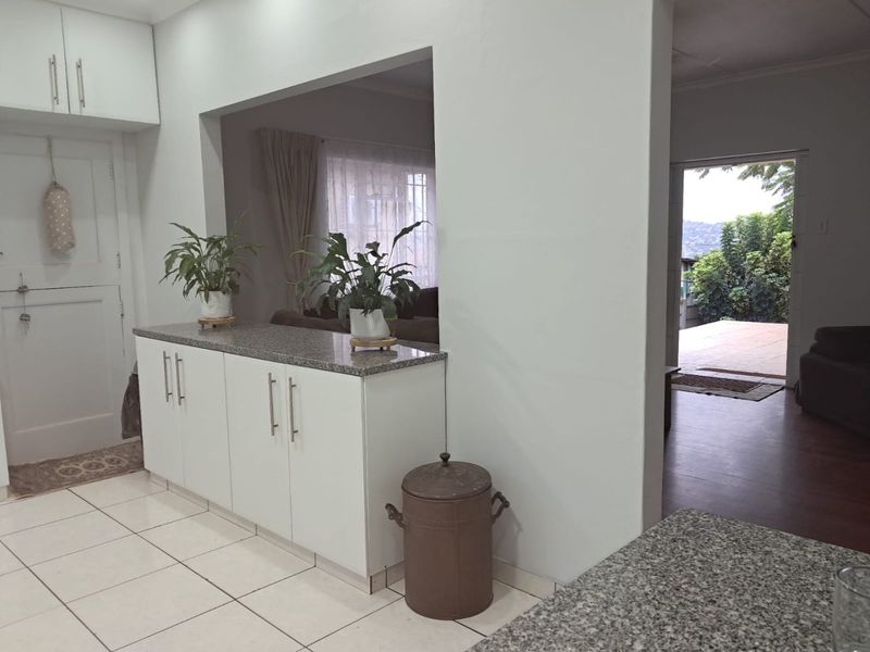 A functional kitchen area featuring white cabinetry, granite countertops, and tiled flooring, with an open-plan layout connecting to the adjacent living space.