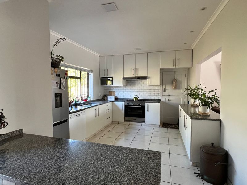 A functional kitchen featuring white cabinetry, granite countertops, a subway tile backsplash, and integrated appliances with tiled flooring throughout.