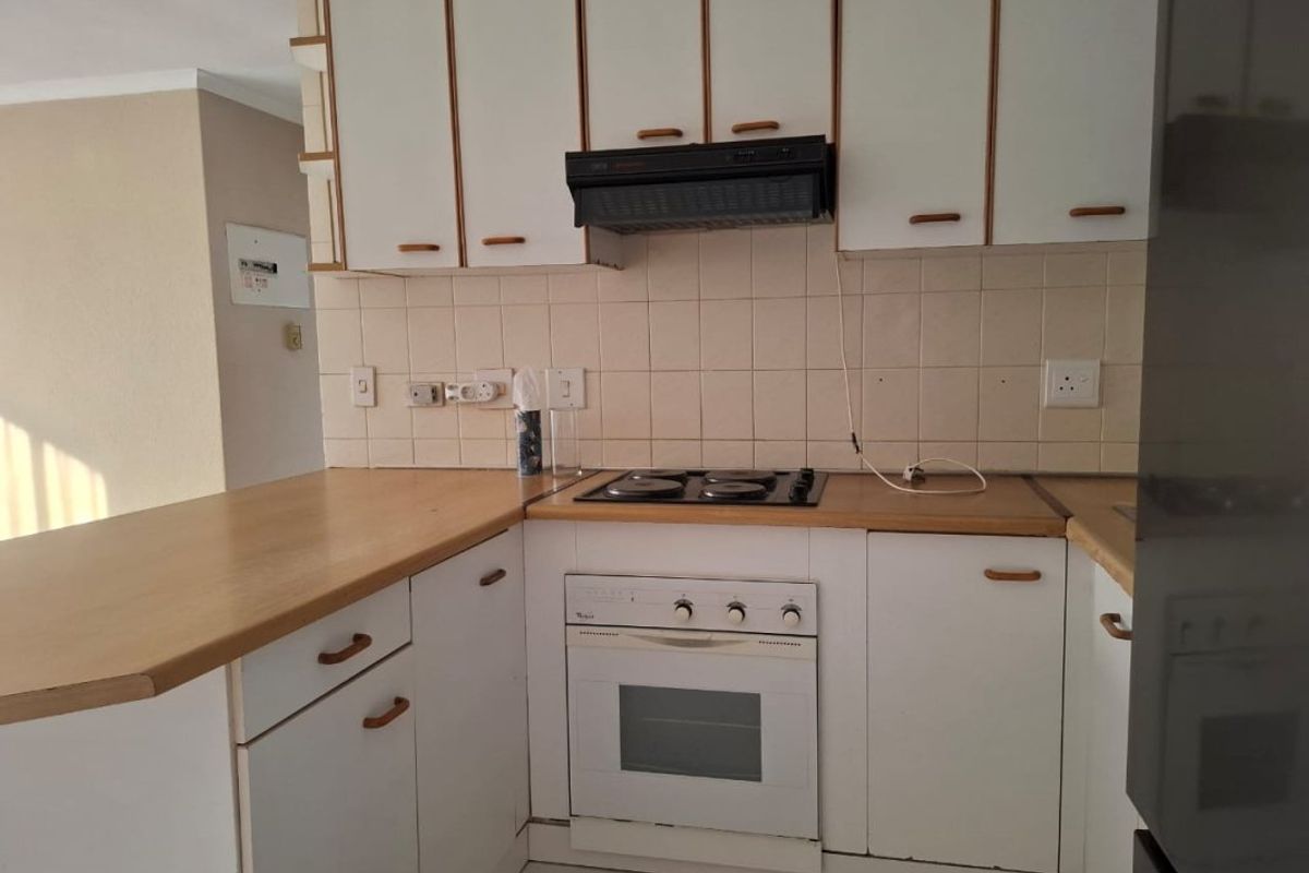 A compact kitchen featuring white cabinetry, laminate countertops, a built-in oven, and an electric hob with an extractor fan.