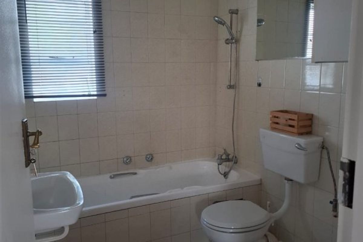 A functional bathroom featuring a bathtub with shower attachment, a wall-mounted basin, and a standard toilet, finished with neutral ceramic wall and floor tiles.