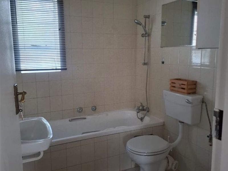 A functional bathroom featuring a bathtub with shower attachment, a wall-mounted basin, and a standard toilet, finished with neutral ceramic wall and floor tiles.