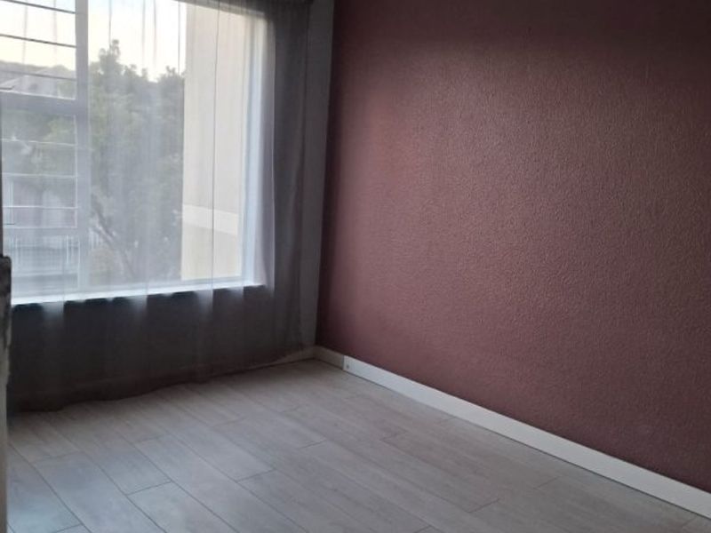 A bright, empty bedroom featuring light-toned laminate flooring, a dark accent wall, and a window fitted with security burglar bars.
