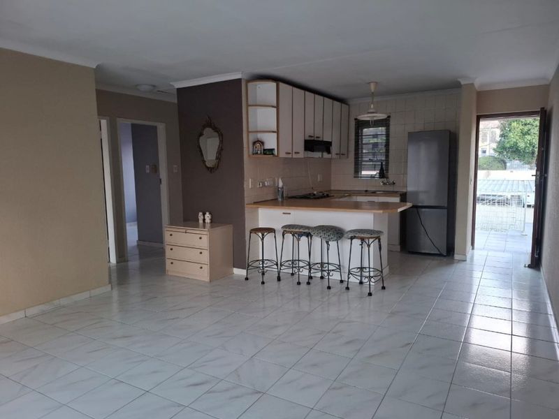Open plan living area featuring tiled flooring and a functional kitchen with breakfast bar, cabinetry, and integrated hob, leading to an outdoor patio area.