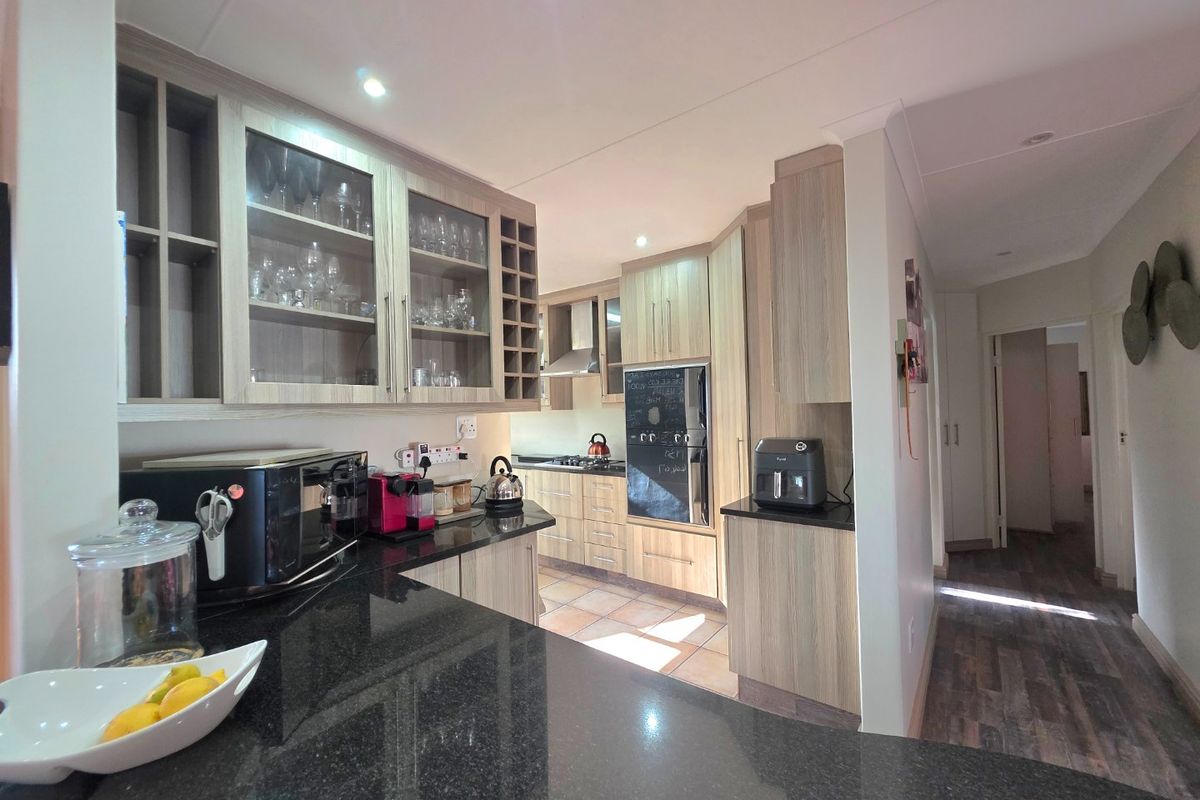 Modern kitchen featuring light wood cabinetry, dark granite countertops, built-in oven, gas hob, and integrated glass-fronted display units.
