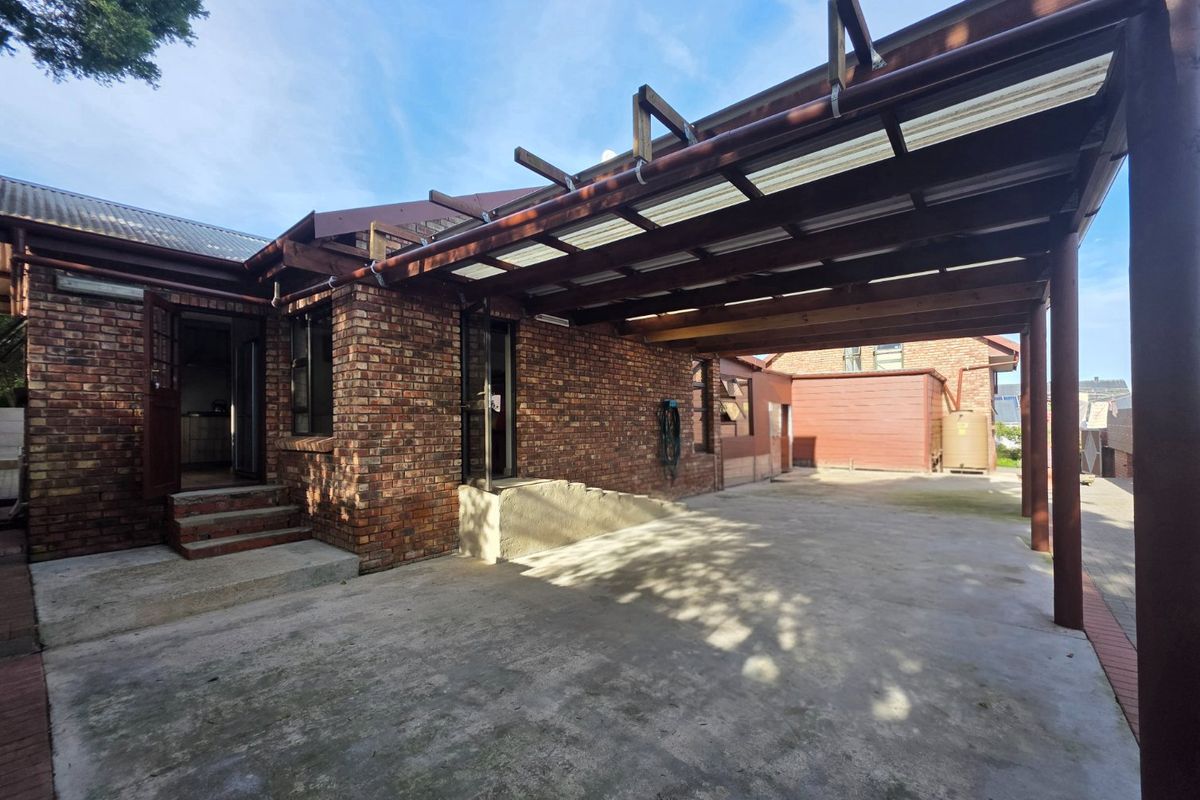 Rear exterior view featuring a brick facade, a covered patio area with a timber pergola, and concrete flooring.
