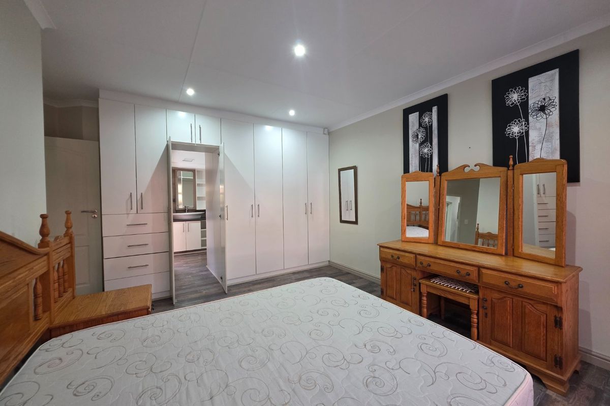 Spacious bedroom featuring extensive built-in cabinetry, recessed lighting, and direct access to an en-suite bathroom with modern laminate flooring throughout.