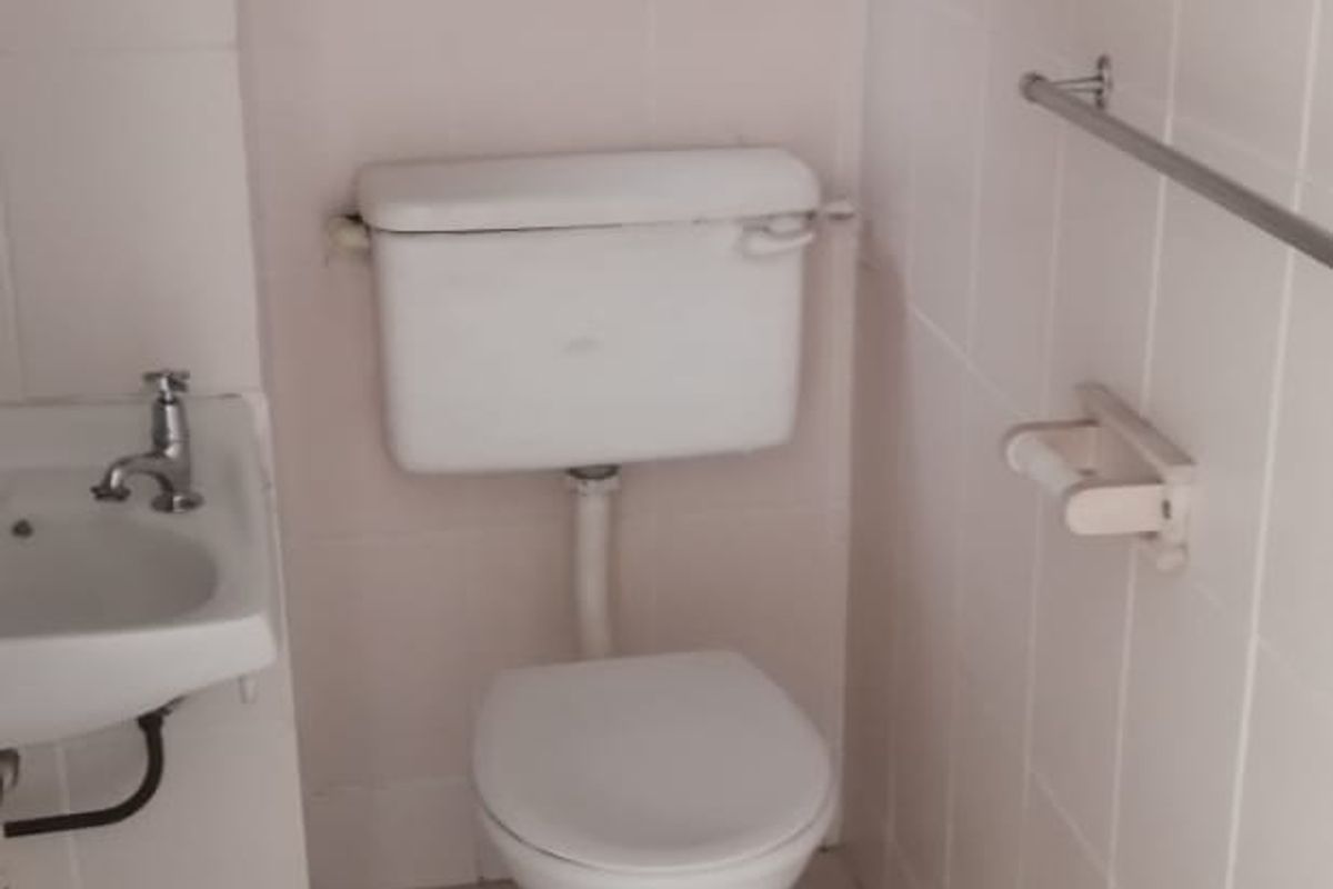 A compact, dated bathroom featuring a standard toilet, wall-mounted basin, and full-height wall tiling. The space is functional but requires cosmetic updates.