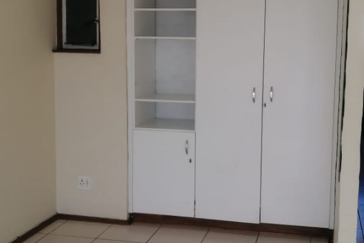 An empty bedroom featuring white built-in cupboards with integrated shelving and neutral tiled flooring.