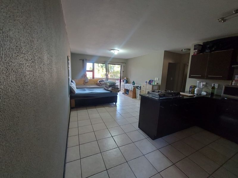 Open-plan living area featuring tiled flooring, a functional kitchen with built-in cabinetry and gas hob, and access to an outdoor space via sliding doors.