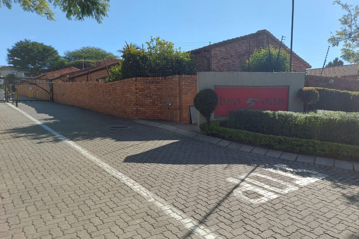 Street view of the complex entrance featuring a brick boundary wall, electric fencing, and paved driveway access.
