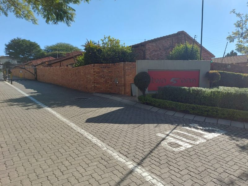 Street view of the complex entrance featuring a brick boundary wall, electric fencing, and paved driveway access.