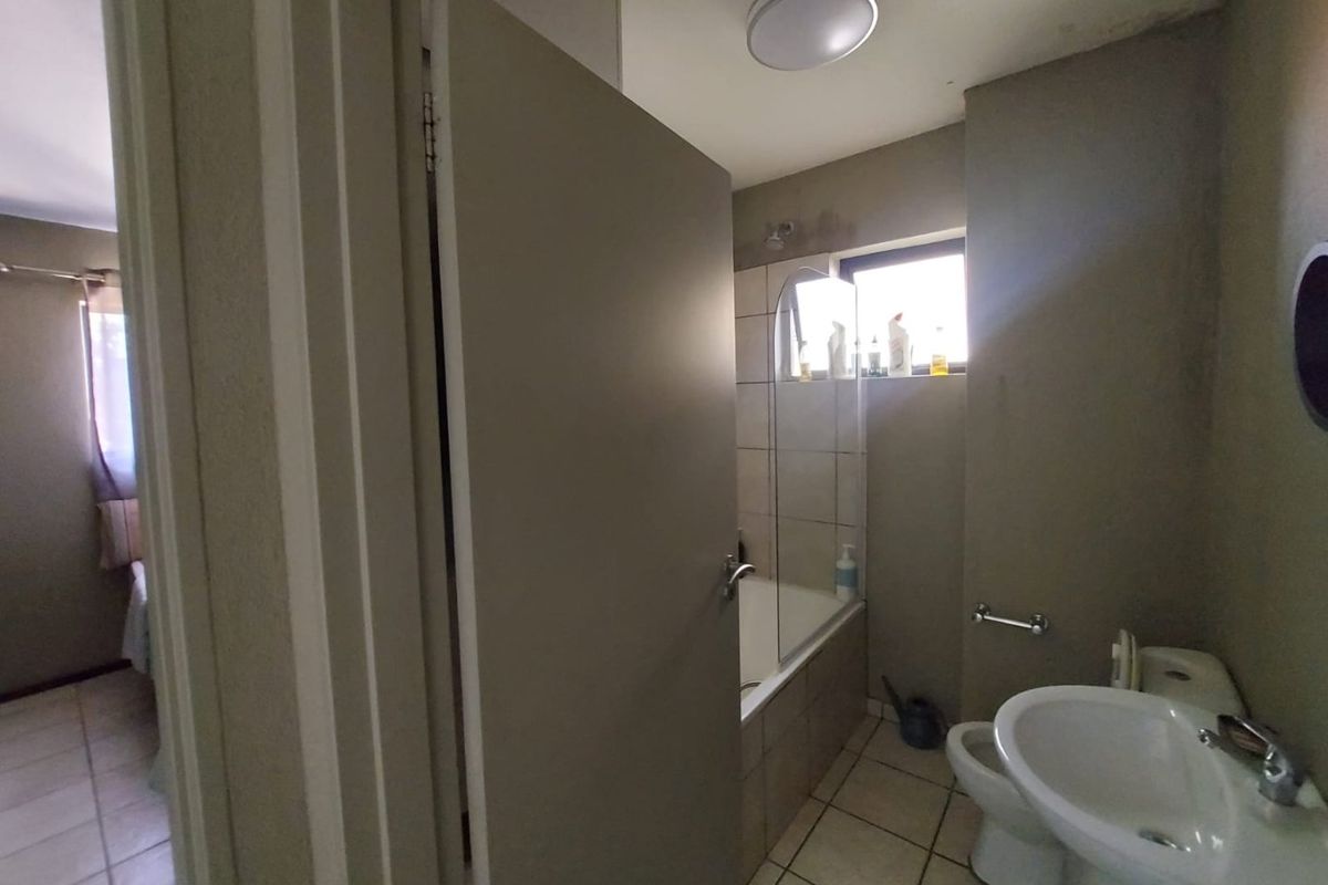 A functional bathroom featuring a bathtub with a glass screen, pedestal basin, and toilet, with tiled flooring and neutral wall finishes.