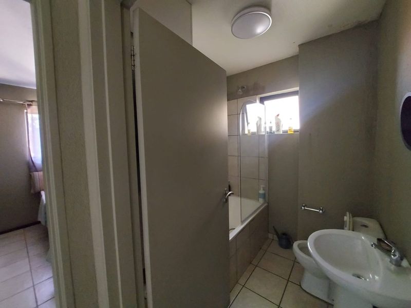 A functional bathroom featuring a bathtub with a glass screen, pedestal basin, and toilet, with tiled flooring and neutral wall finishes.