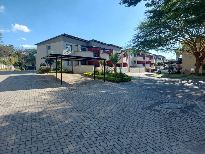 Exterior view of a modern apartment complex featuring paved driveway access, covered carports, and well-maintained landscaped garden areas.