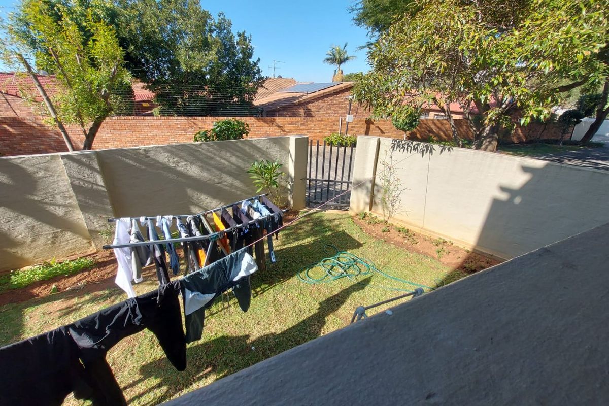 A private rear garden area featuring a lawn, perimeter boundary walls, and a secure metal access gate.