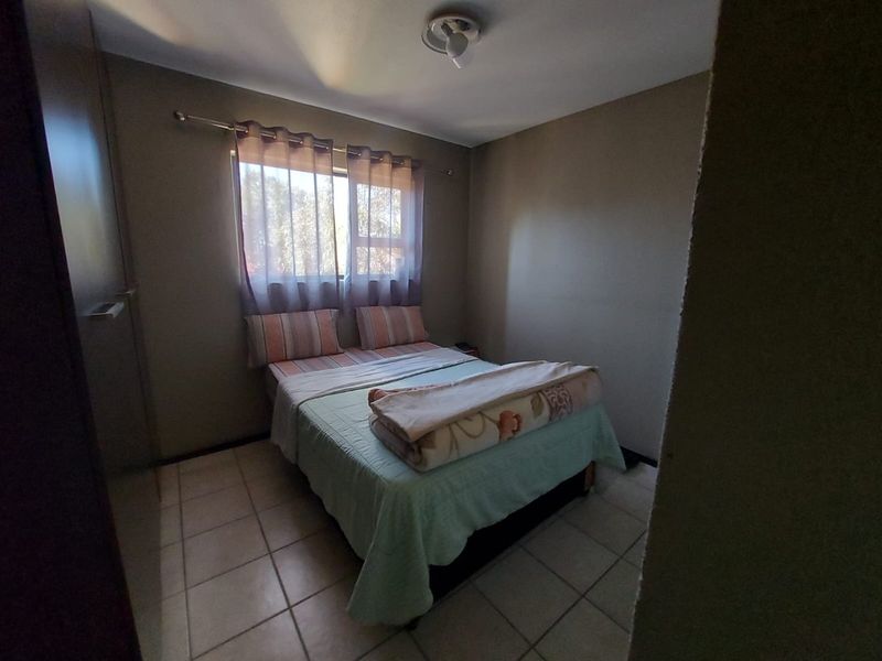 A functional bedroom featuring tiled flooring, a built-in cupboard, and a window providing natural light.