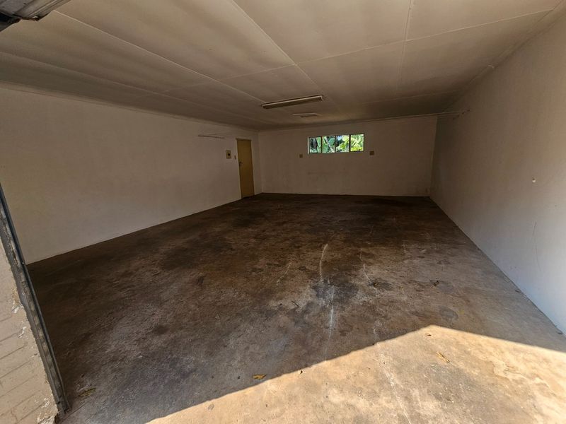 A spacious, empty garage featuring a concrete floor, fluorescent lighting, and a single access door, providing ample storage or parking space.