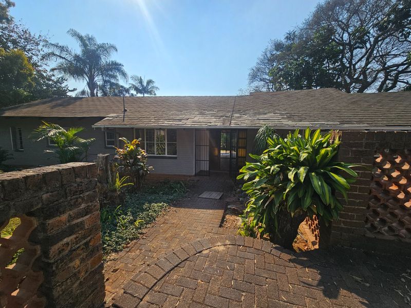 Front view of a single-story house featuring a brick paved entrance path, brick boundary walls, and a shingle roof.