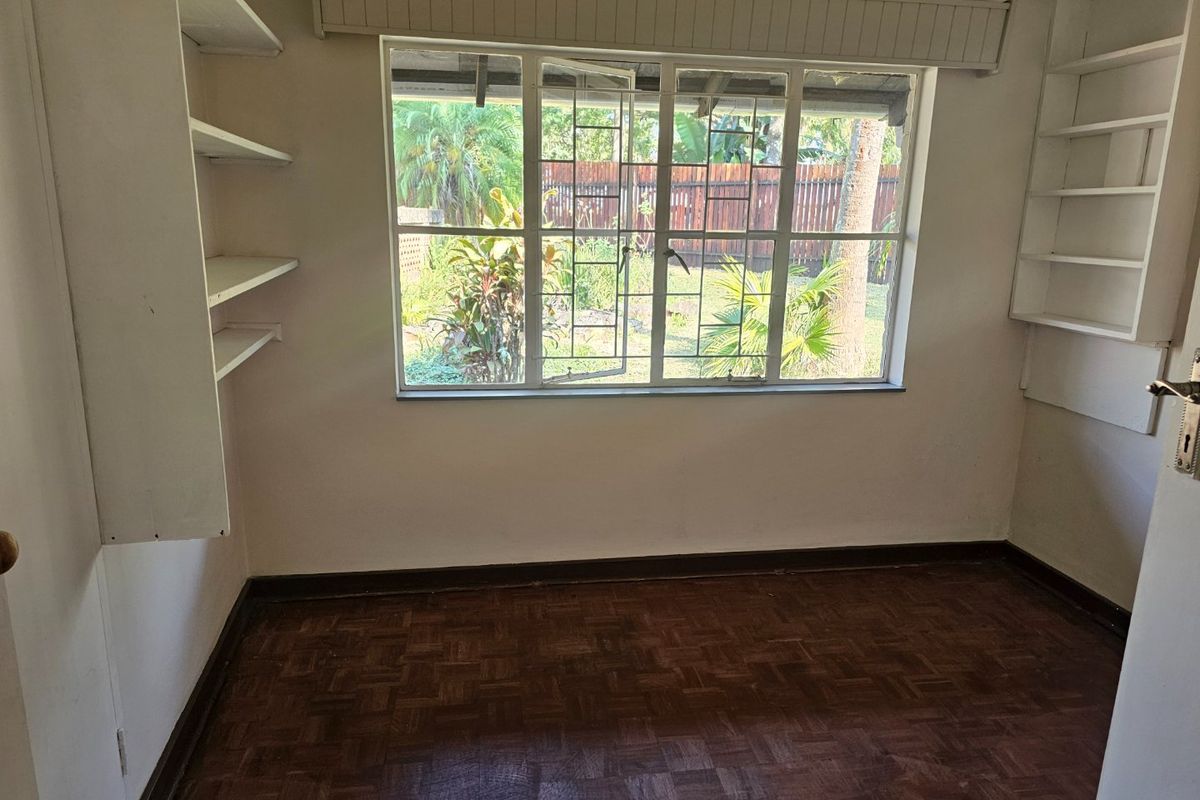 An empty bedroom featuring original parquet flooring, built-in wall shelving, and a steel-framed window overlooking the rear garden.