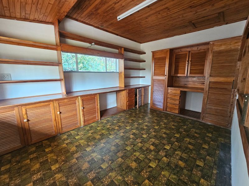 A vacant home office featuring extensive built-in wooden cabinetry, shelving, and a timber-clad ceiling, offering a functional workspace with significant potential for modernization.