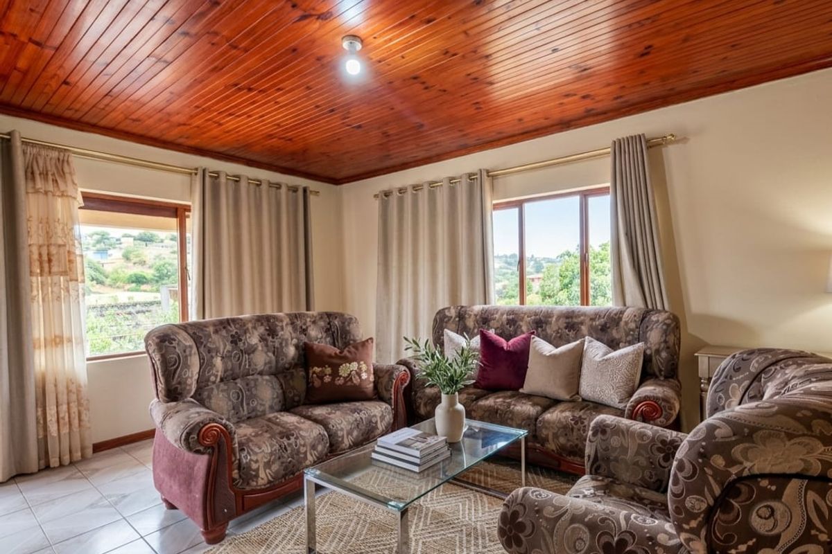 A comfortable living room featuring a warm timber tongue and groove ceiling, tiled flooring, and large windows providing natural light and exterior views.