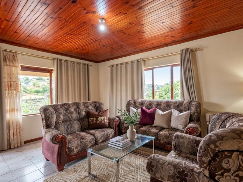 A comfortable living room featuring a warm timber tongue and groove ceiling, tiled flooring, and large windows providing natural light and exterior views.
