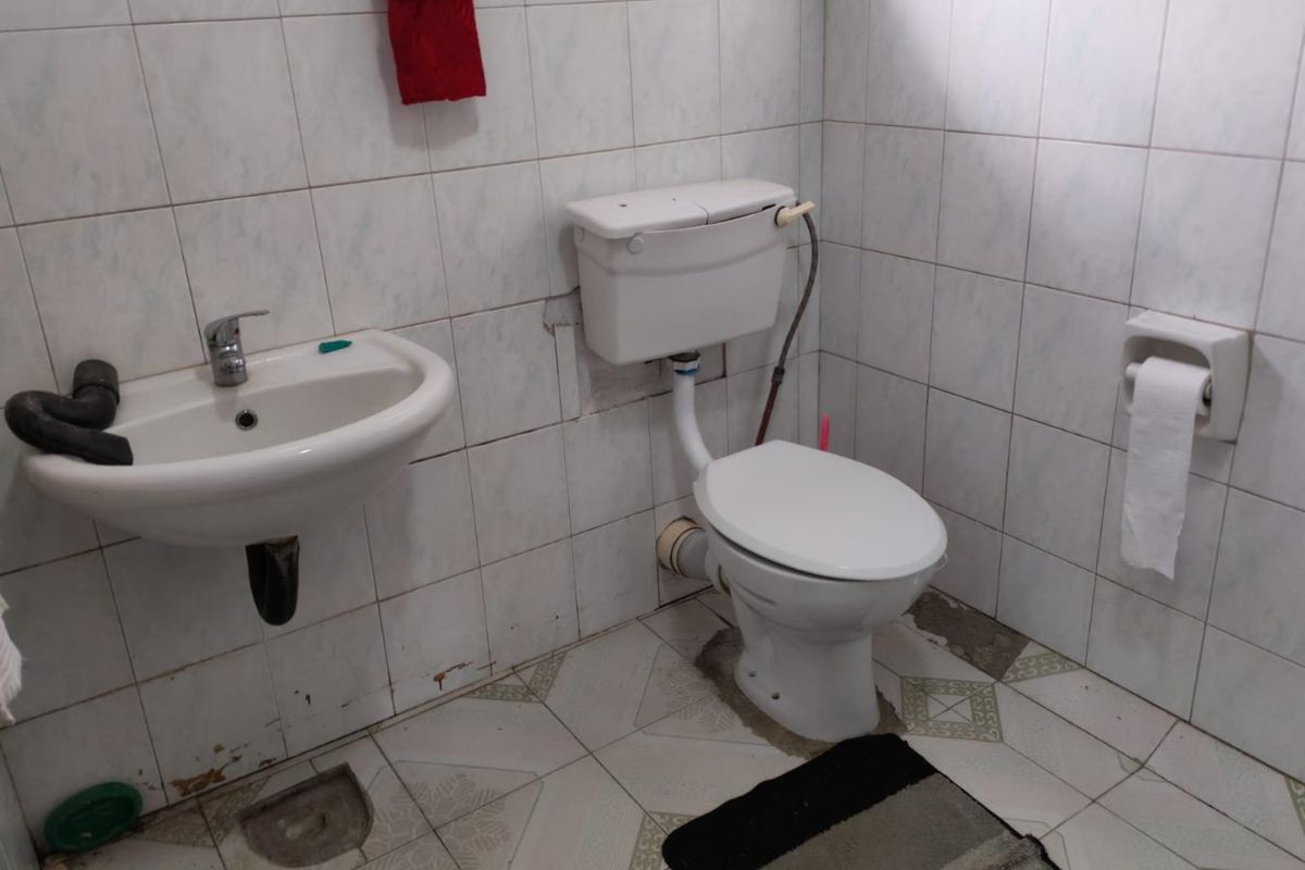 A functional bathroom featuring a wall-mounted basin and standard toilet, finished with tiled walls and flooring, currently requiring maintenance and cosmetic updates.