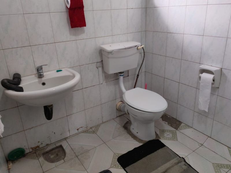 A functional bathroom featuring a wall-mounted basin and standard toilet, finished with tiled walls and flooring, currently requiring maintenance and cosmetic updates.