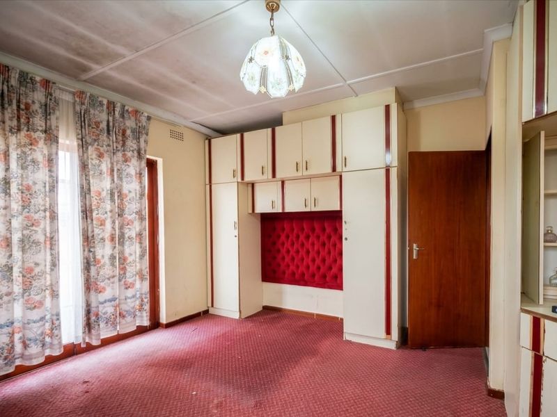 A bedroom featuring built-in cupboards with a red upholstered headboard section, carpeted flooring, and a ceiling light fixture.