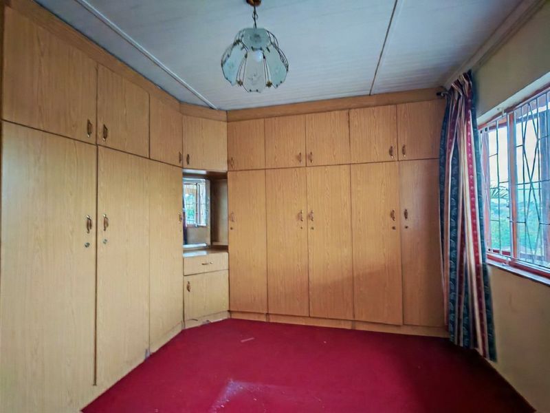 A bedroom featuring extensive built-in wooden cabinetry and a vanity unit, with red carpeting and security bars on the window.