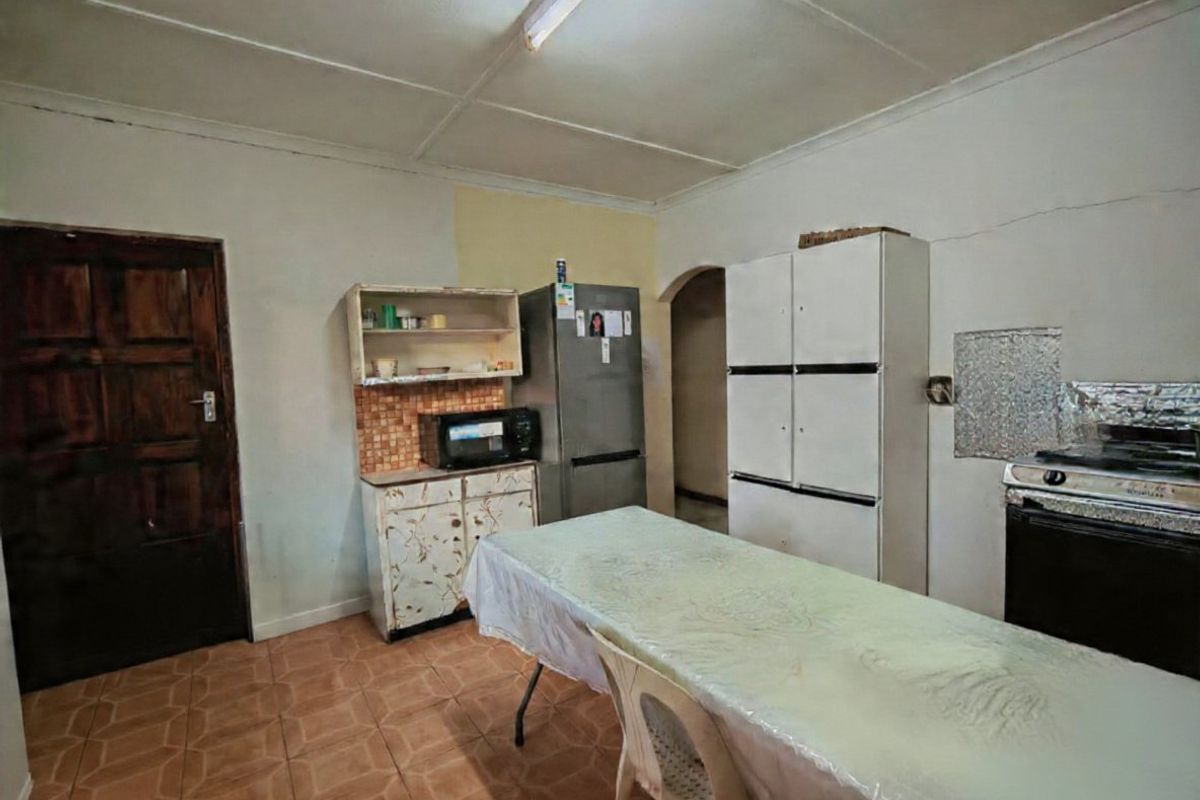A dated kitchen area featuring tiled flooring, basic cabinetry, and a tiled backsplash, requiring cosmetic updates and repairs to wall finishes.