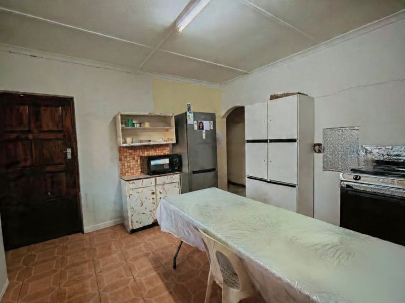 A dated kitchen area featuring tiled flooring, basic cabinetry, and a tiled backsplash, requiring cosmetic updates and repairs to wall finishes.