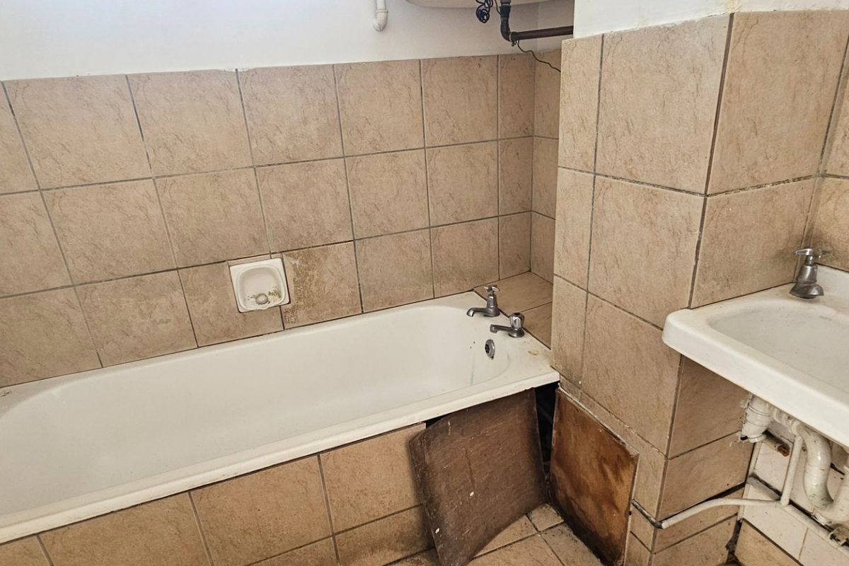A dated bathroom featuring a bathtub and wall-mounted basin with exposed plumbing, requiring renovation and cosmetic updates to improve functionality and aesthetic appeal.