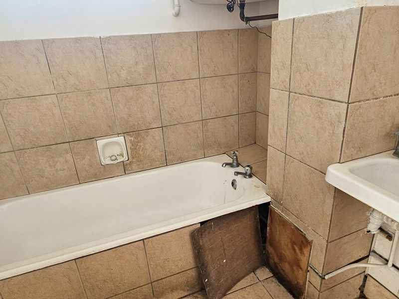 A dated bathroom featuring a bathtub and wall-mounted basin with exposed plumbing, requiring renovation and cosmetic updates to improve functionality and aesthetic appeal.