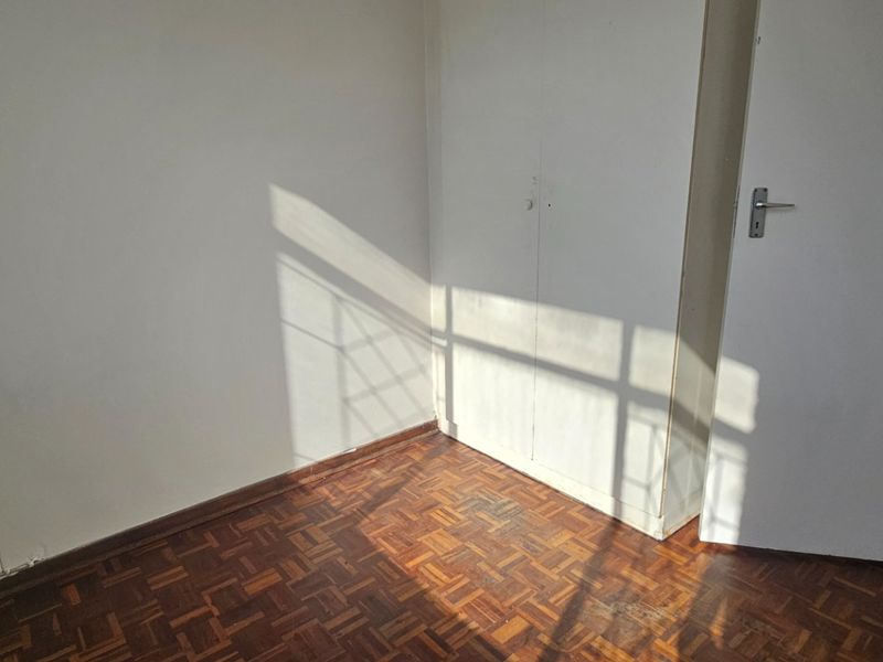 An empty bedroom featuring classic parquet flooring and a built-in cupboard, offering a clean and neutral space ready for personalization.