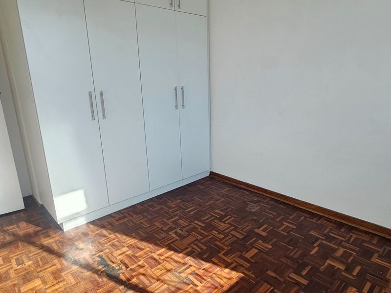 An empty bedroom featuring classic parquet flooring and white built-in cupboards, offering a blank canvas for personalization.