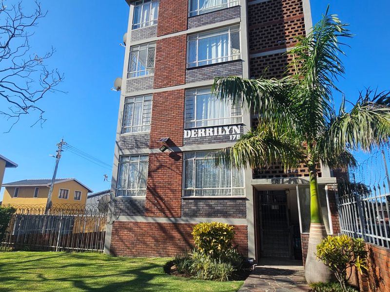Front elevation of the Derrilyn apartment building featuring a brick facade, secure perimeter fencing with razor wire, and a well-maintained garden entrance.