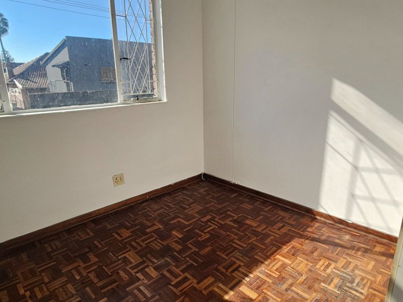 A vacant bedroom featuring original parquet flooring and a window with security bars, offering a blank canvas for potential updates.