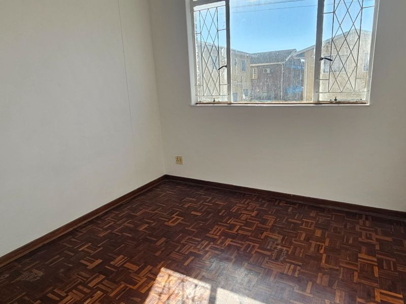 An empty bedroom featuring traditional parquet flooring and a window fitted with security bars, offering a blank canvas for potential updates.