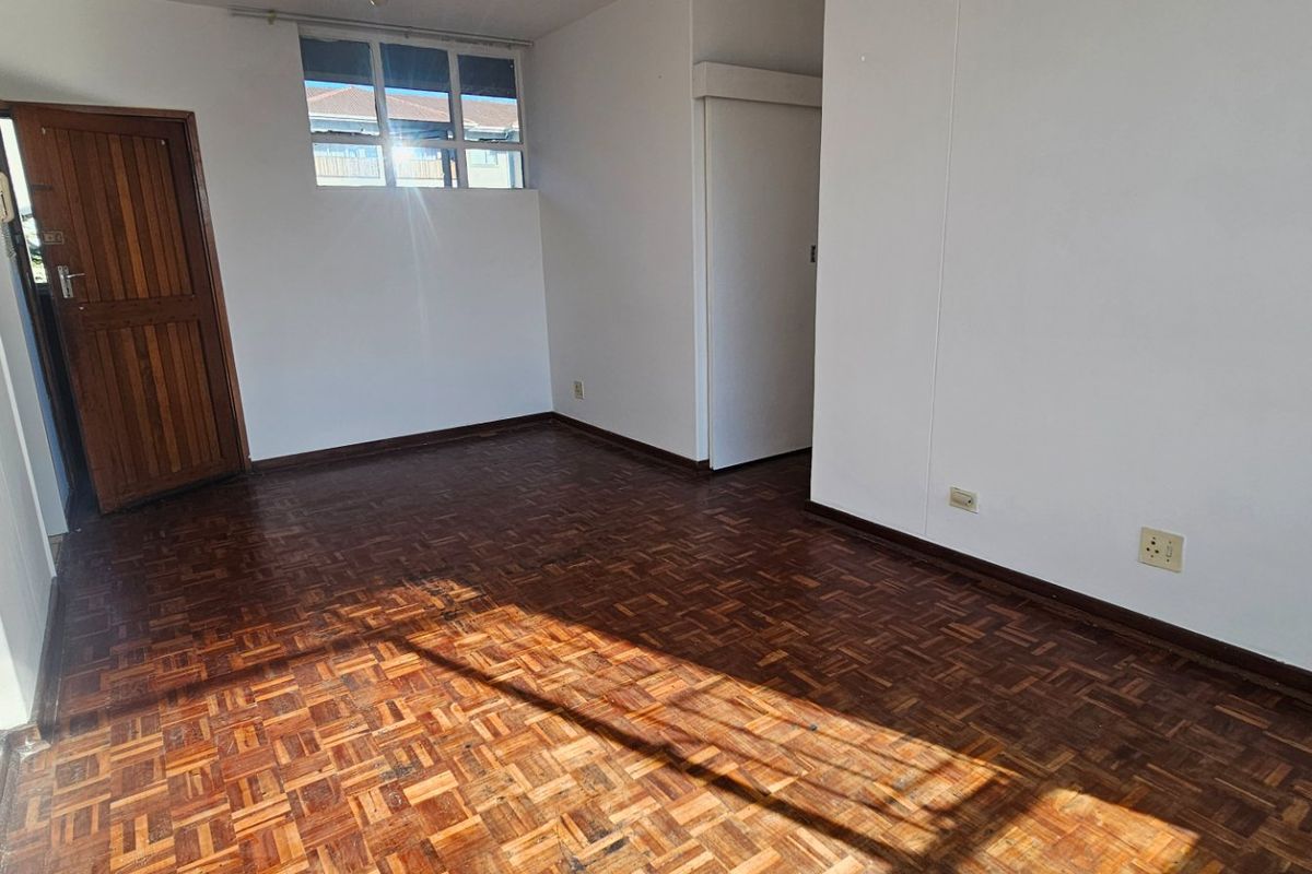 An empty bedroom featuring traditional parquet flooring, a timber door, and neutral white walls, offering a blank canvas for personalization.