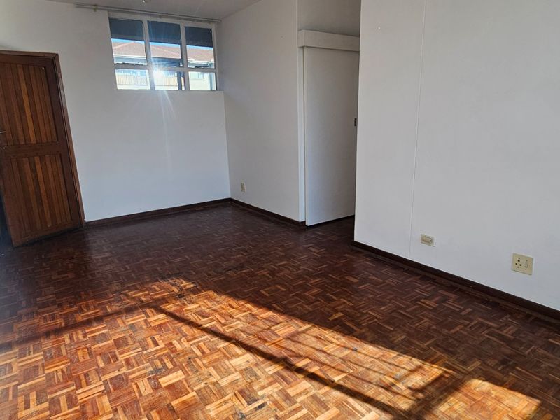 An empty bedroom featuring traditional parquet flooring, a timber door, and neutral white walls, offering a blank canvas for personalization.