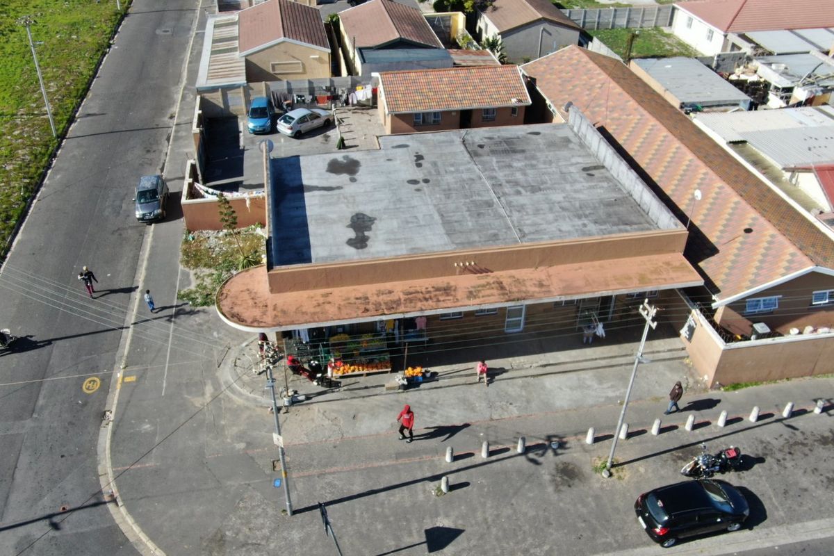 Aerial view of a commercial property featuring a flat roof, paved frontage with concrete bollards, and surrounding perimeter walls in a suburban setting.