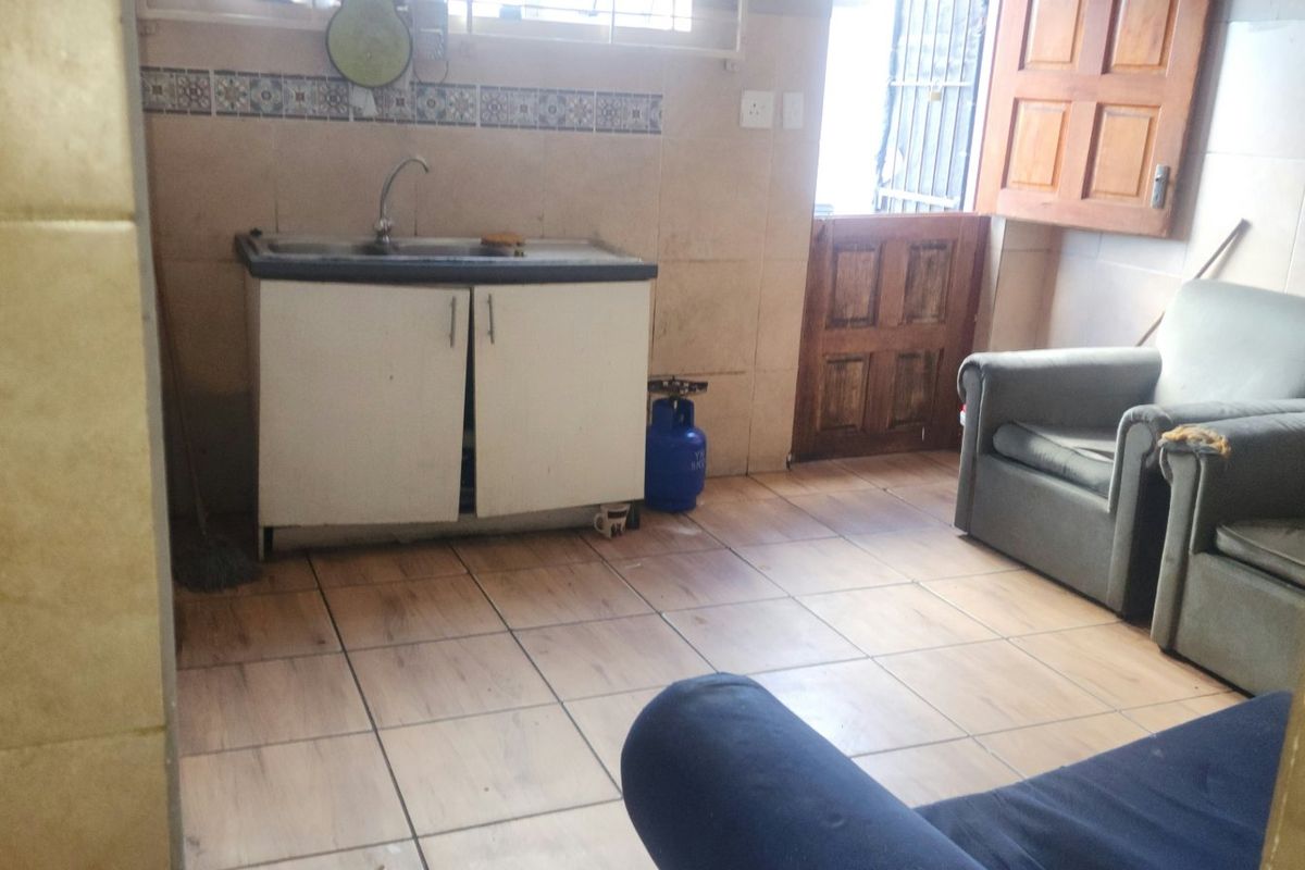 A functional kitchen area featuring tiled walls and flooring, a single sink unit, and direct access to an exterior door.