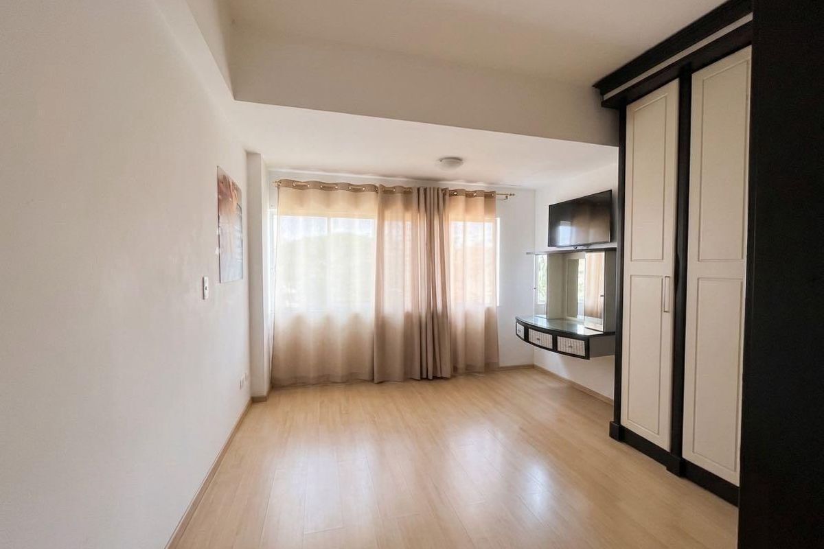 A bright bedroom featuring light laminate flooring, a large built-in wardrobe, and a floating vanity unit.