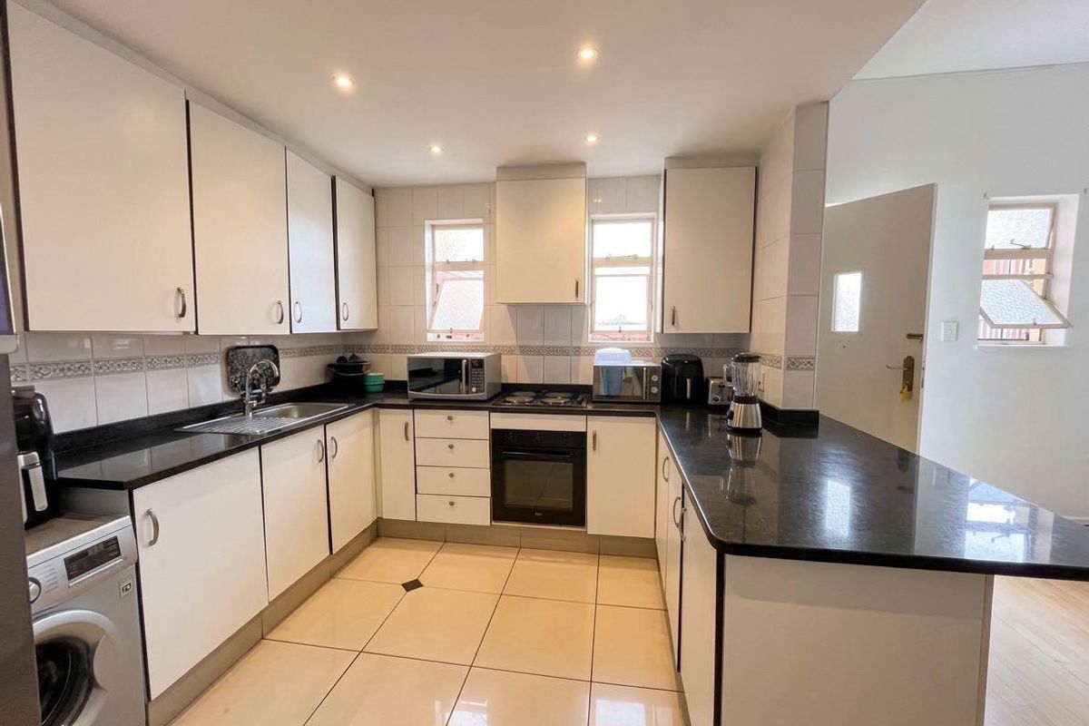A functional kitchen featuring white cabinetry, dark granite countertops, tiled flooring, and integrated appliances including an oven and hob.
