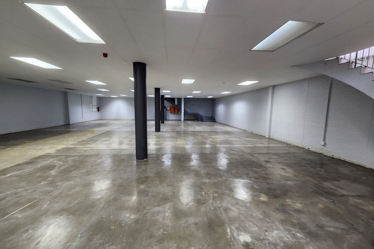 A spacious, open-plan commercial interior featuring polished concrete floors, structural columns, and a suspended ceiling with recessed lighting.
