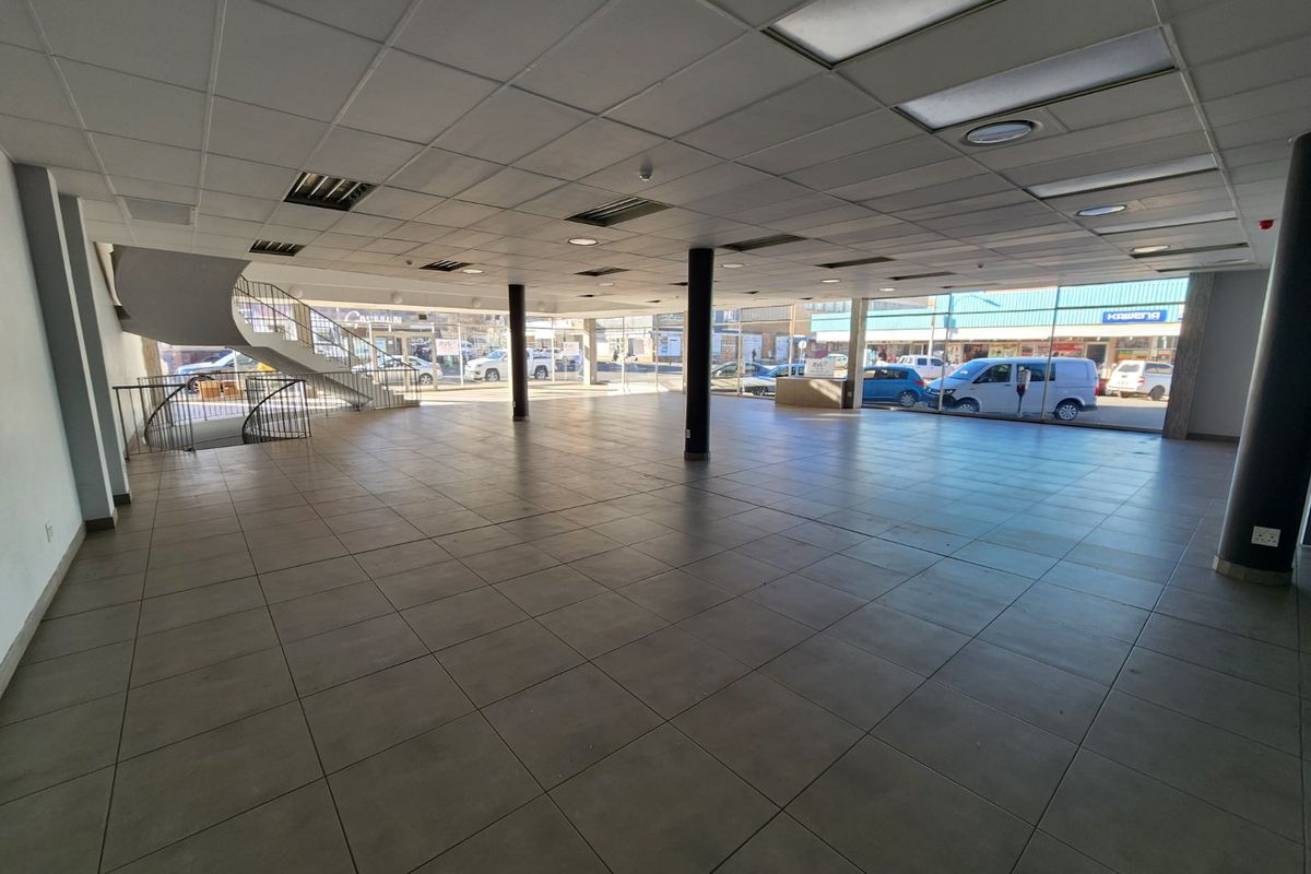 Spacious open-plan commercial retail area featuring large display windows, tiled flooring, a suspended ceiling, and an internal staircase.