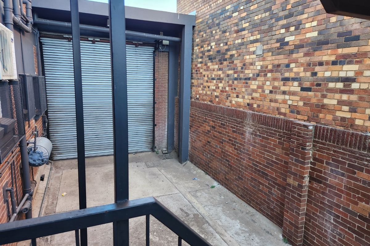 A rear exterior service area featuring a secure roller shutter door, brick walls, and concrete paving, suitable for commercial access or utility use.