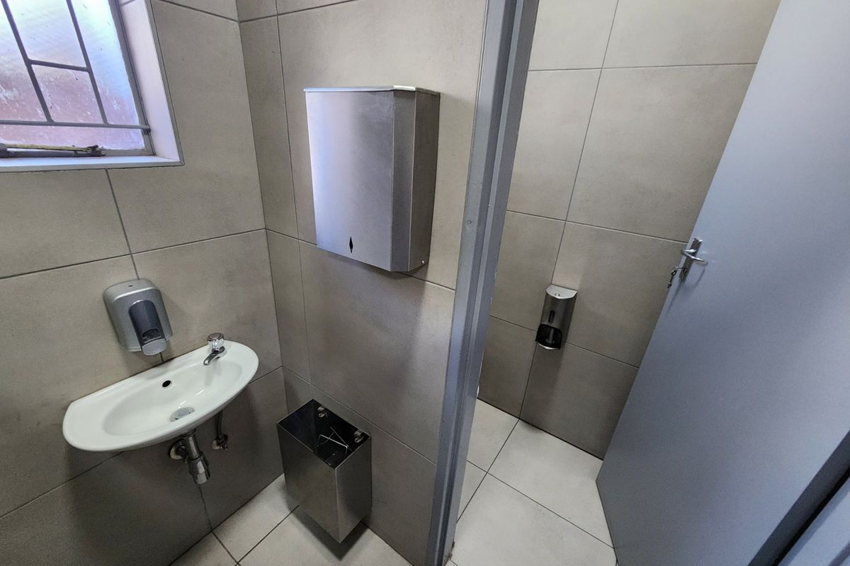 A functional commercial restroom featuring tiled surfaces, a wall-mounted basin, and stainless steel fixtures including a soap dispenser and paper towel holder.